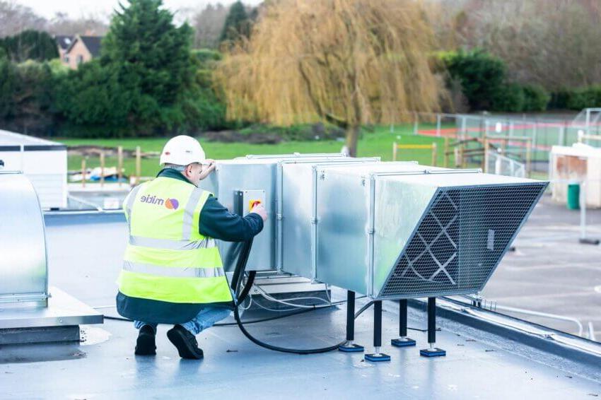 Mitie engineer in high-vis and hard hat working on a rooftop ventilation system